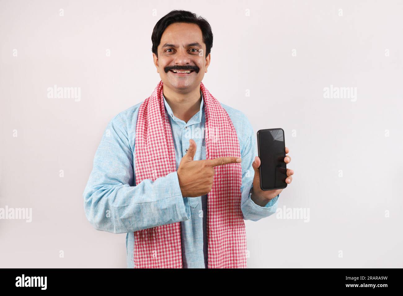 Ritratto di un contadino indiano nel concetto rurale dell'India. Espressioni funky sfondo bianco. Allegro agricoltore che mostra lo schermo del telefono cellulare utilizzando la tecnologia Foto Stock