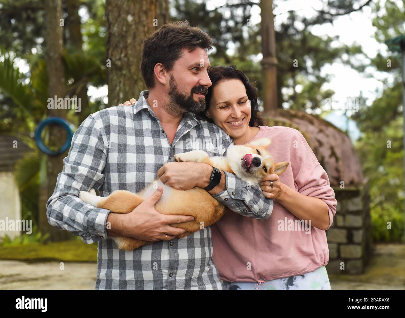 Uomo e donna dalla barba felici che reggono il loro corgi gallese e sorridono Foto Stock