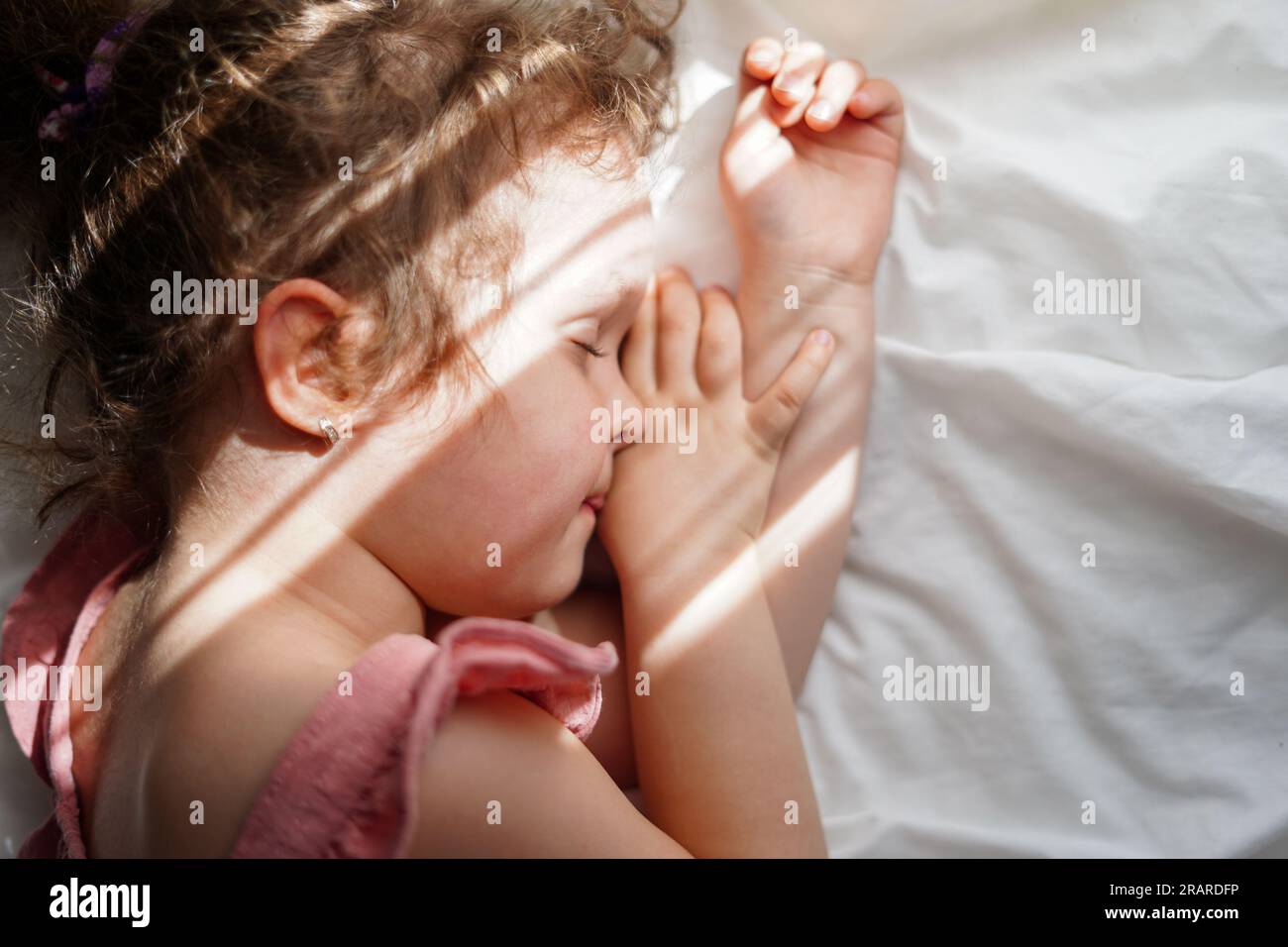 Una bambina carina che dorme sul letto con le luci del sole a casa Foto Stock