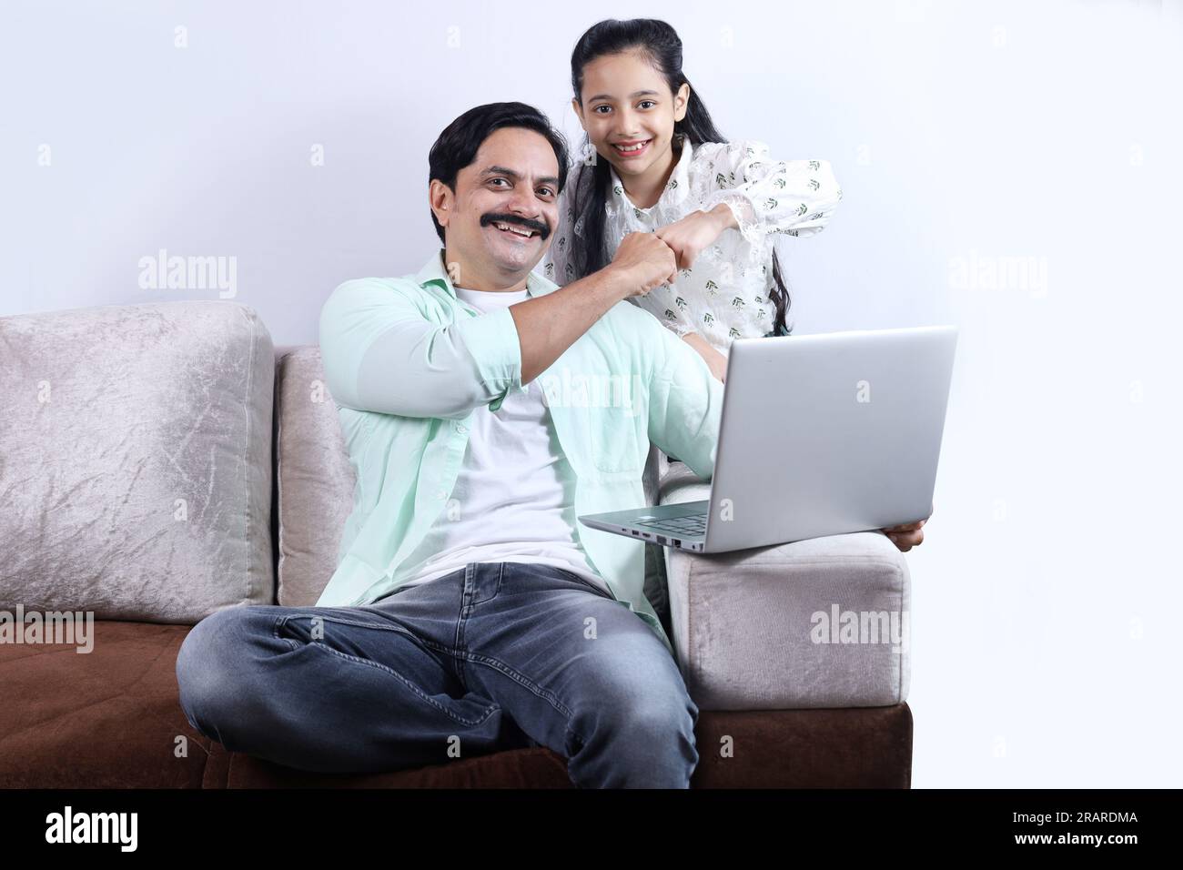 Felice famiglia indiana di padre e figlia single che fa surf con un computer portatile e si diverte piacevolmente insieme. La famiglia sta indagando sul portatile. Foto Stock