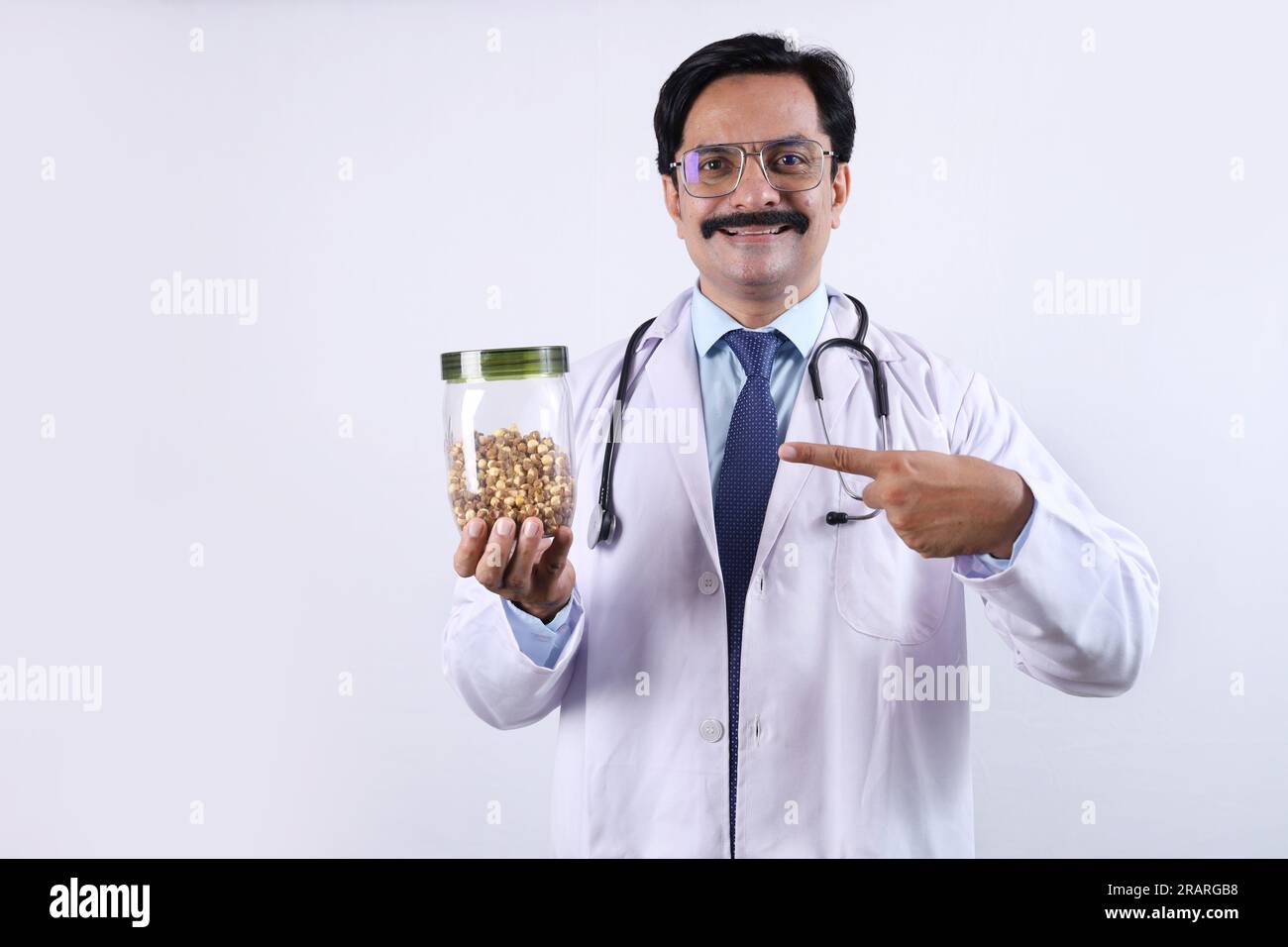 Indiano fiducioso Dottore tenendo un vaso in mano e suggerendo di mangiare fresco e sano. Il medico in piedi su uno sfondo bianco. Foto Stock