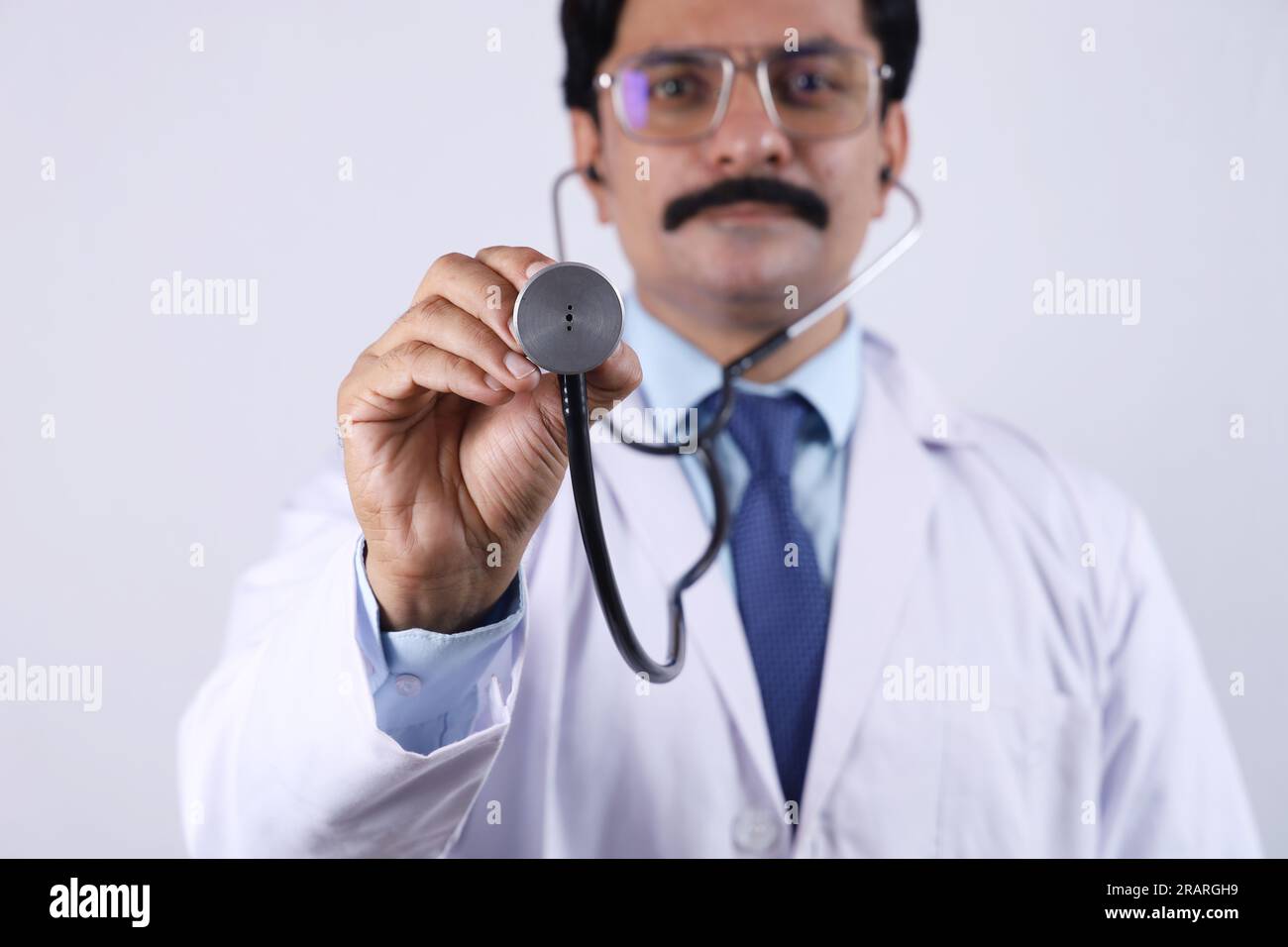 Ritratto di un medico indiano felice in uniforme che mostra stetoscopio e specifiche. Stetoscopio. Dottore in baffi. Medico e sanitario. Foto Stock