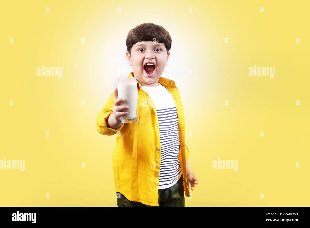 Ritratto di un bambino premuroso che tiene in mano un bicchiere di latte con molta sicurezza e il piccolo campione sta dando un sorriso molto cattivo e sicuro. Foto Stock