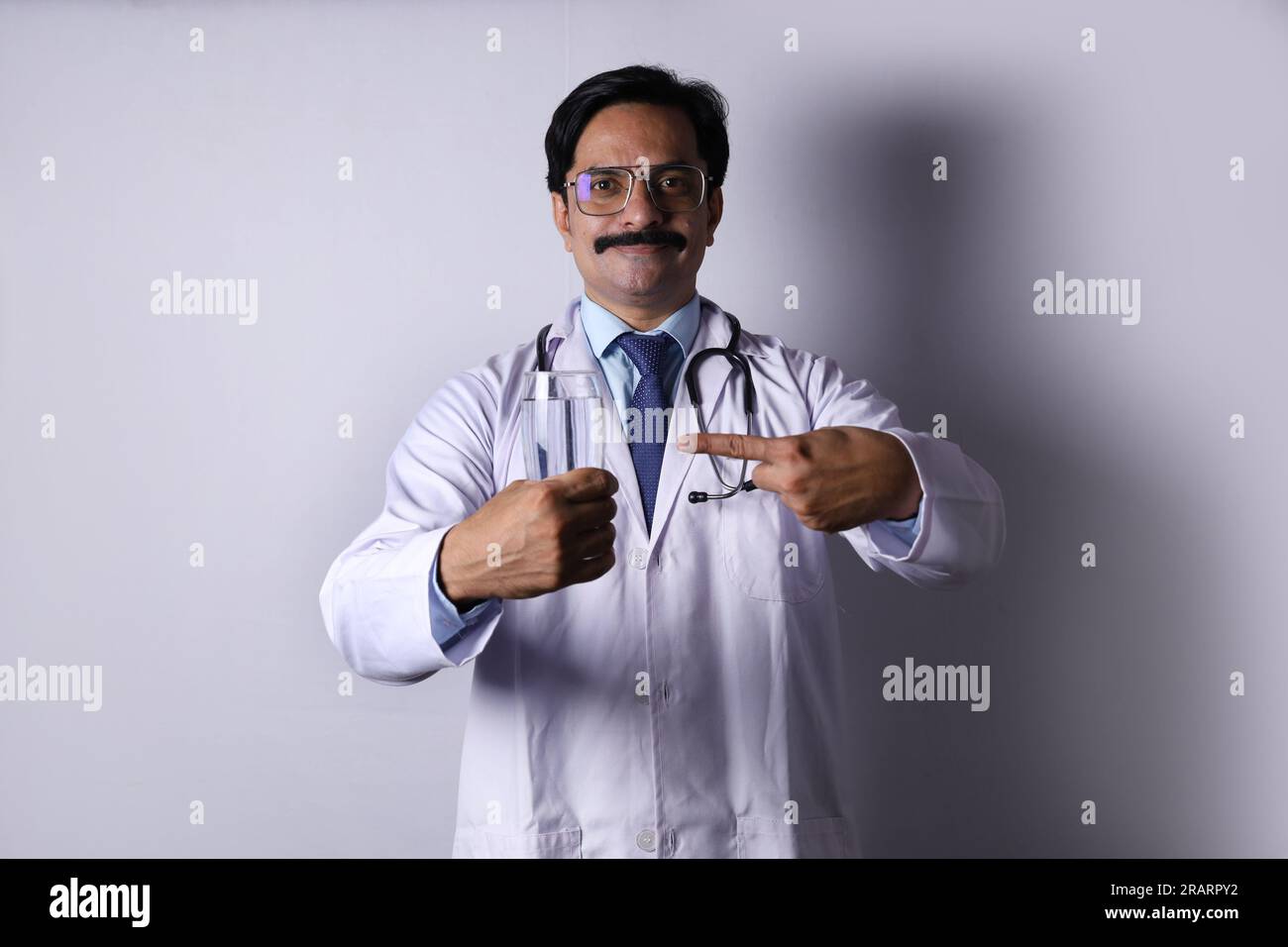 Indiano fiducioso Dottore tenendo in mano una bevanda salutare e suggerendo di bere fresco e sano. Il medico in piedi su uno sfondo bianco. Foto Stock