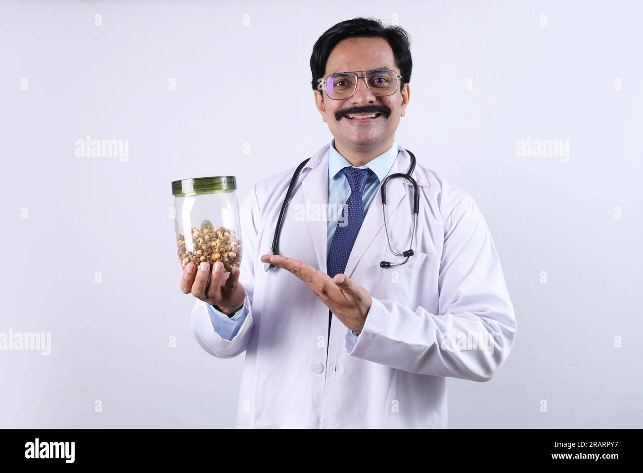 Indiano fiducioso Dottore tenendo un vaso in mano e suggerendo di mangiare fresco e sano. Il medico in piedi su uno sfondo bianco. Foto Stock