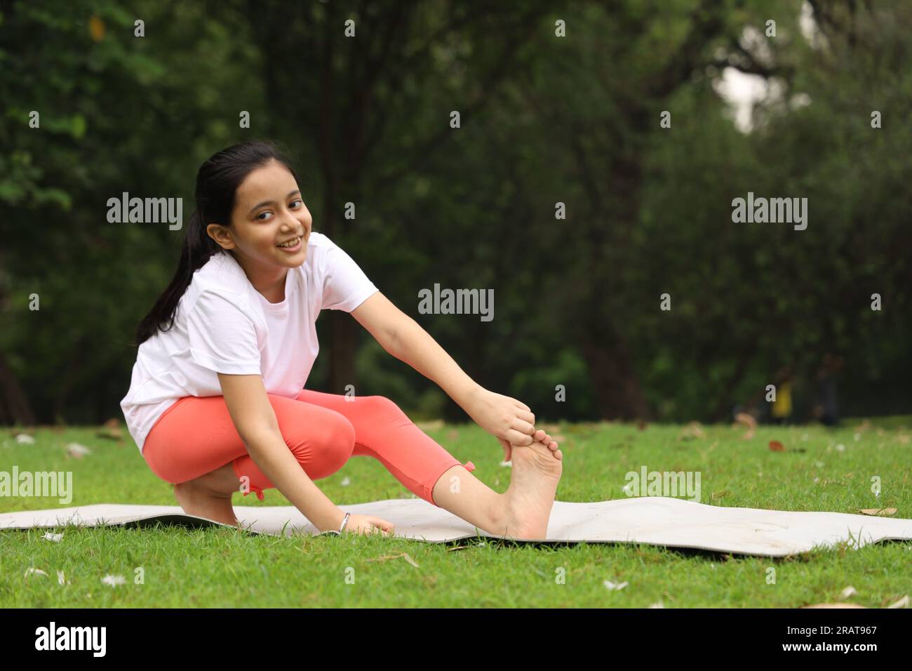 Un bambino che fa esercizi di yoga la mattina presto in un parco pubblico verde. Possiamo vedere le anatre in giro. Il bambino è consapevole della salute. Felice ragazza yoga. Foto Stock