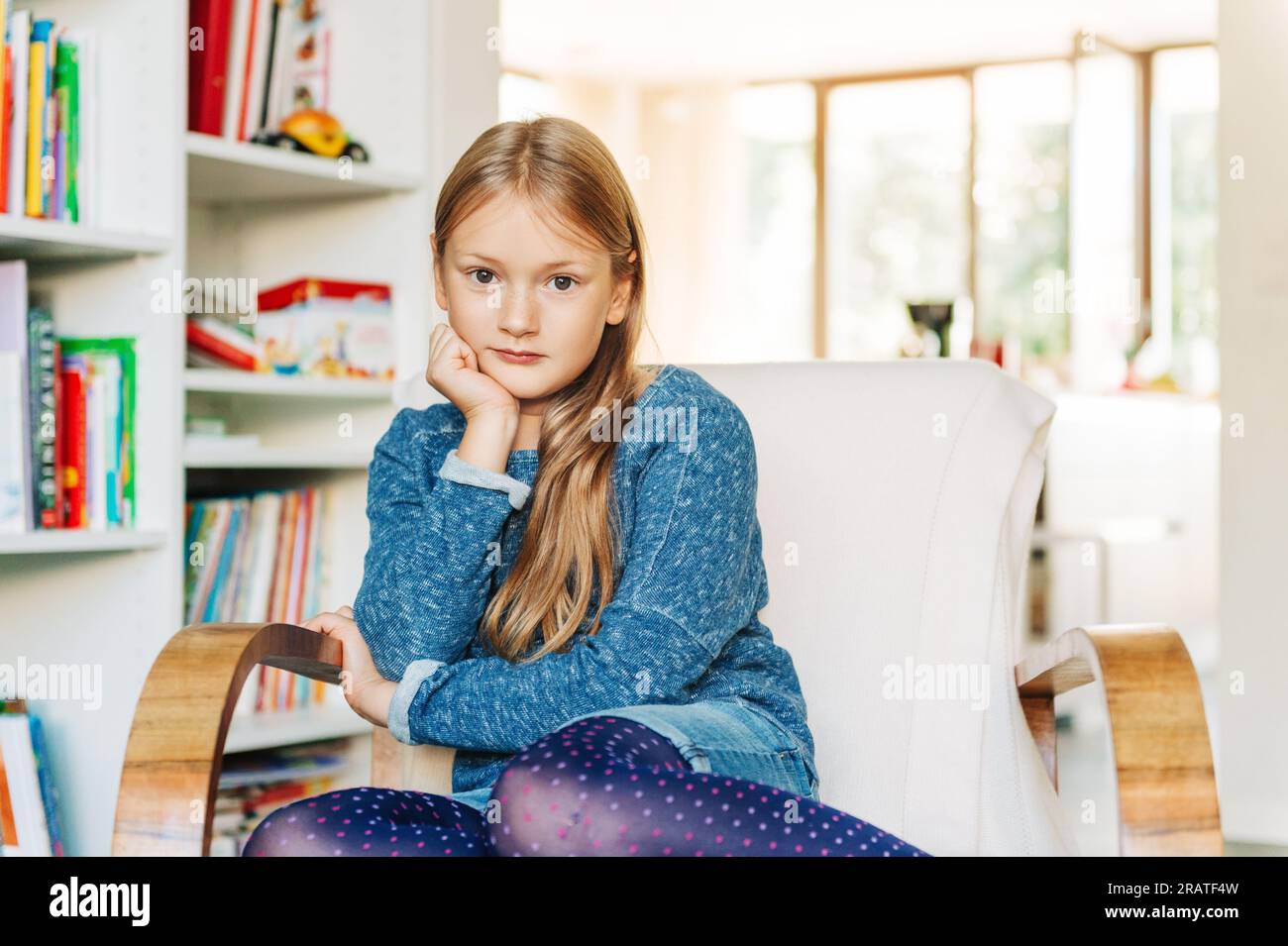 Graziosa bambina seduta su una sedia bianca a casa Foto Stock