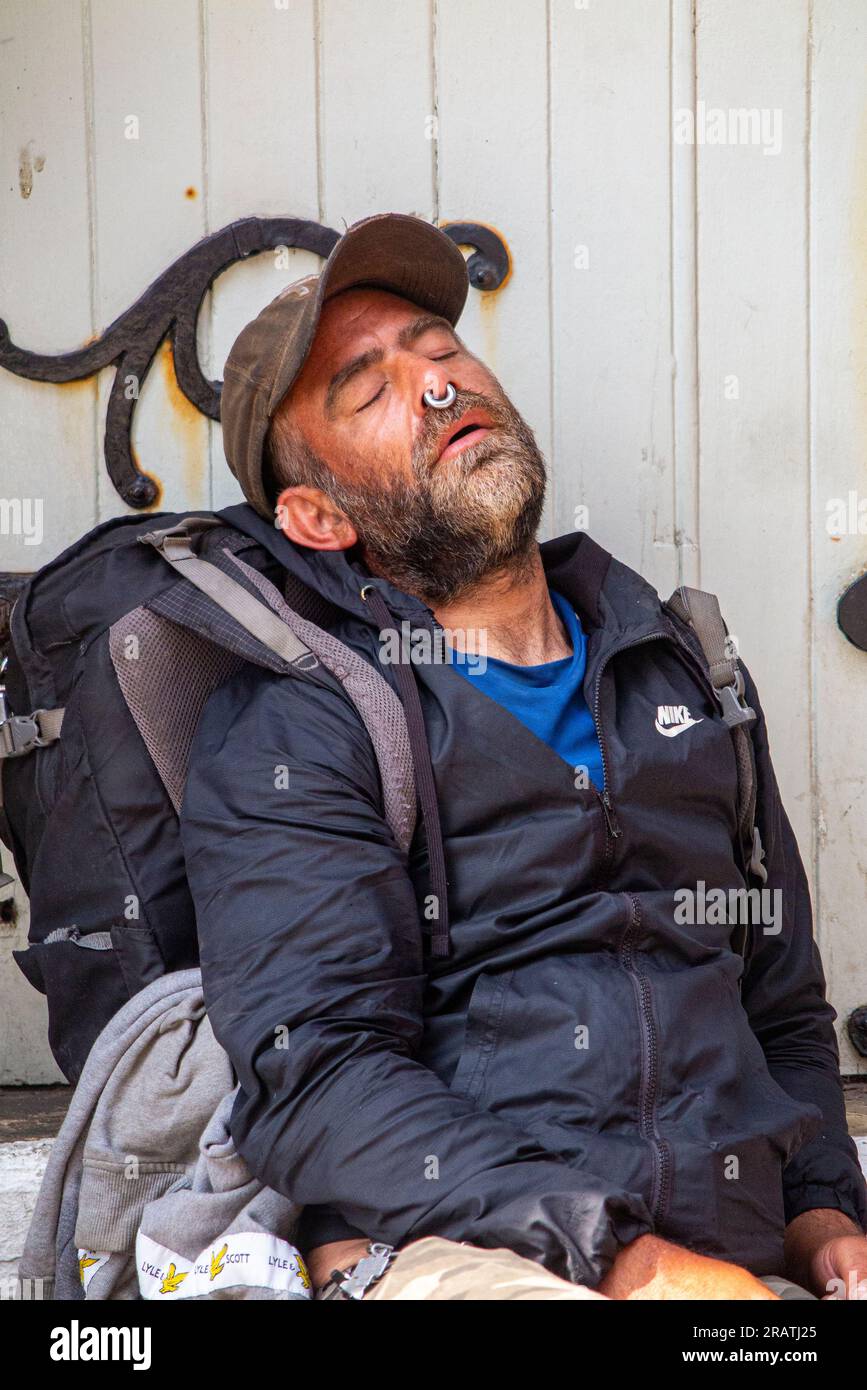 Un uomo con un anello di naso nel setto dorme su alcuni gradini a Brighton Foto Stock