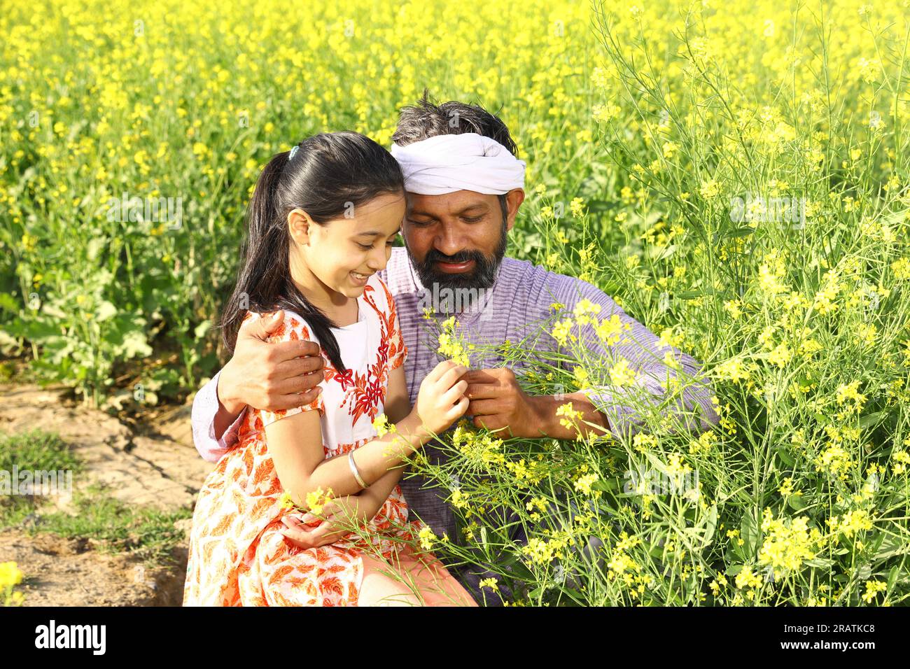 Contadini indiani felici. Padre e figlia in un campo di senape che si godono le fiorenti colture agricole. Fiori di senape gialli. Foto Stock