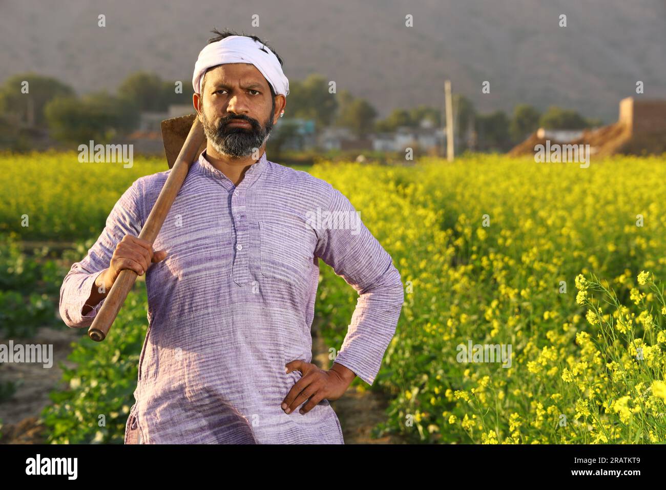 Un contadino indiano arrabbiato con la barba in piedi con una pala in mano che indossa il pigiama Kurta. Foto Stock