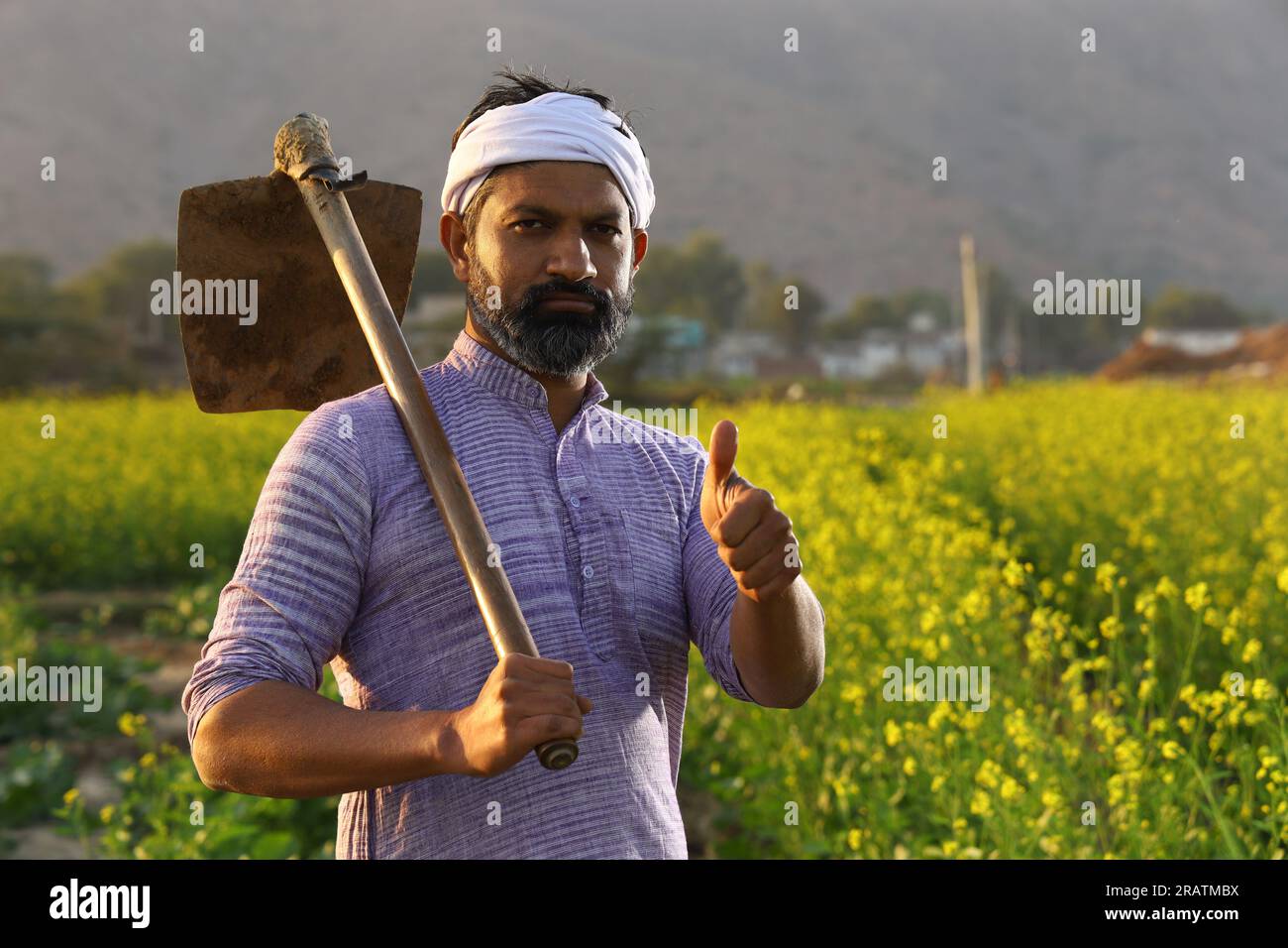 Un contadino indiano arrabbiato con la barba in piedi con una pala in mano che indossa il pigiama Kurta. Foto Stock