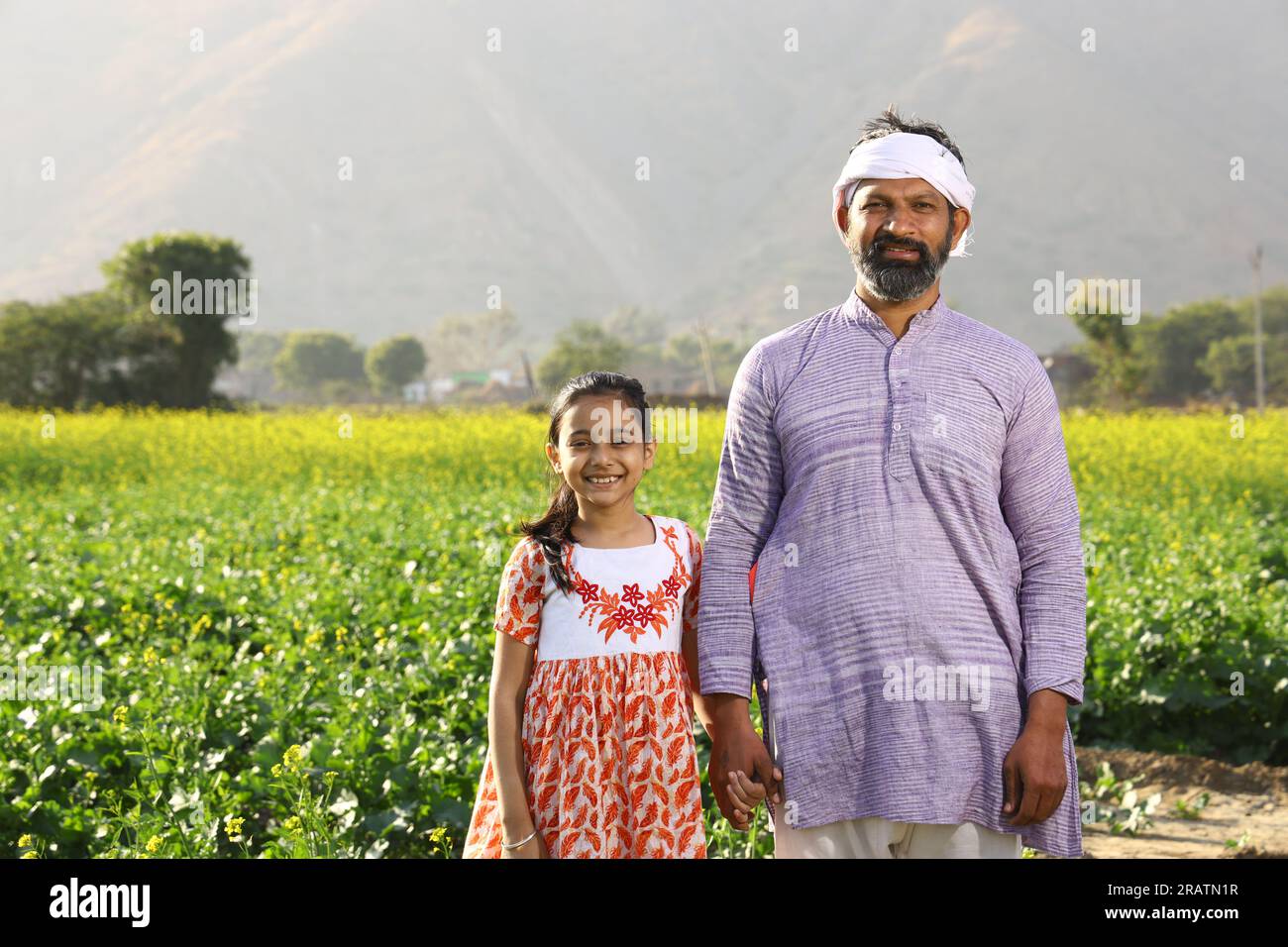 Contadini indiani felici. Padre e figlia in un campo di senape che si godono le fiorenti colture agricole. Fiori di senape gialli. Foto Stock