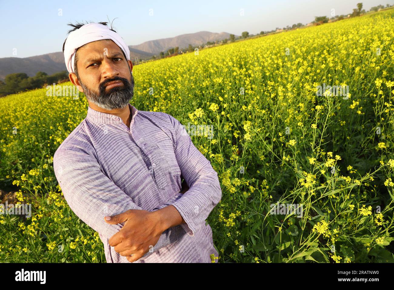 Agricoltore che si sente orgoglioso del suo impegno per la crescita del suo campo. Bellissimo ritratto di un contadino rurale indiano in piedi nel campo di senape. Foto Stock