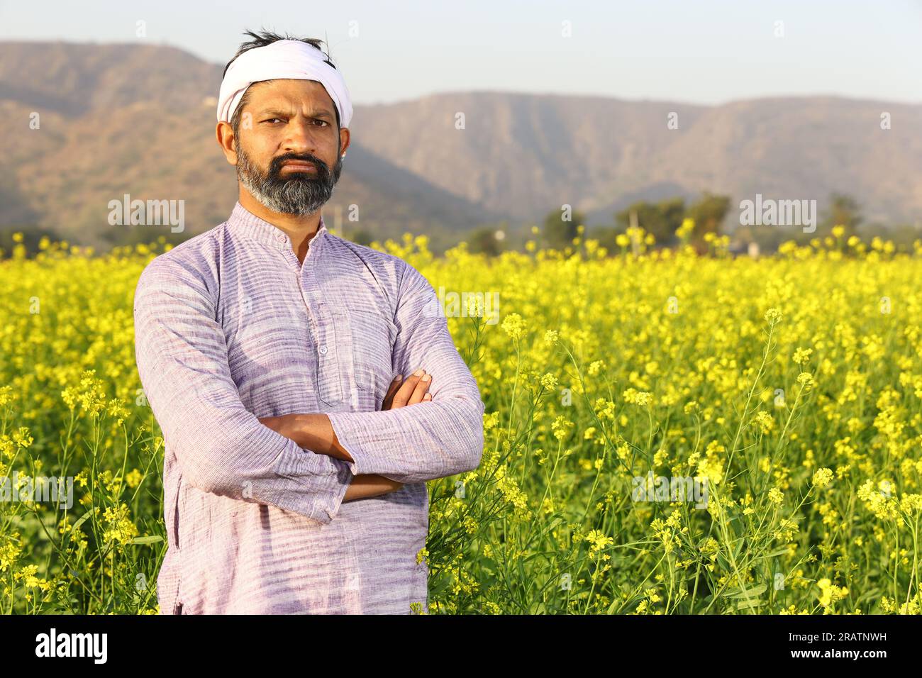 Agricoltore che si sente orgoglioso del suo impegno per la crescita del suo campo. Bellissimo ritratto di un contadino rurale indiano in piedi nel campo di senape. Foto Stock