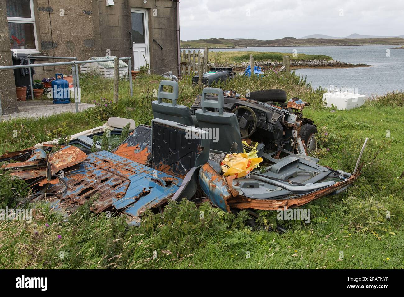 Rusty Relics of an Old Wrecked Car in the Garden Near to the Sea, Ebridi esterne, Western Isles, Scozia, Regno Unito, Gran Bretagna Foto Stock