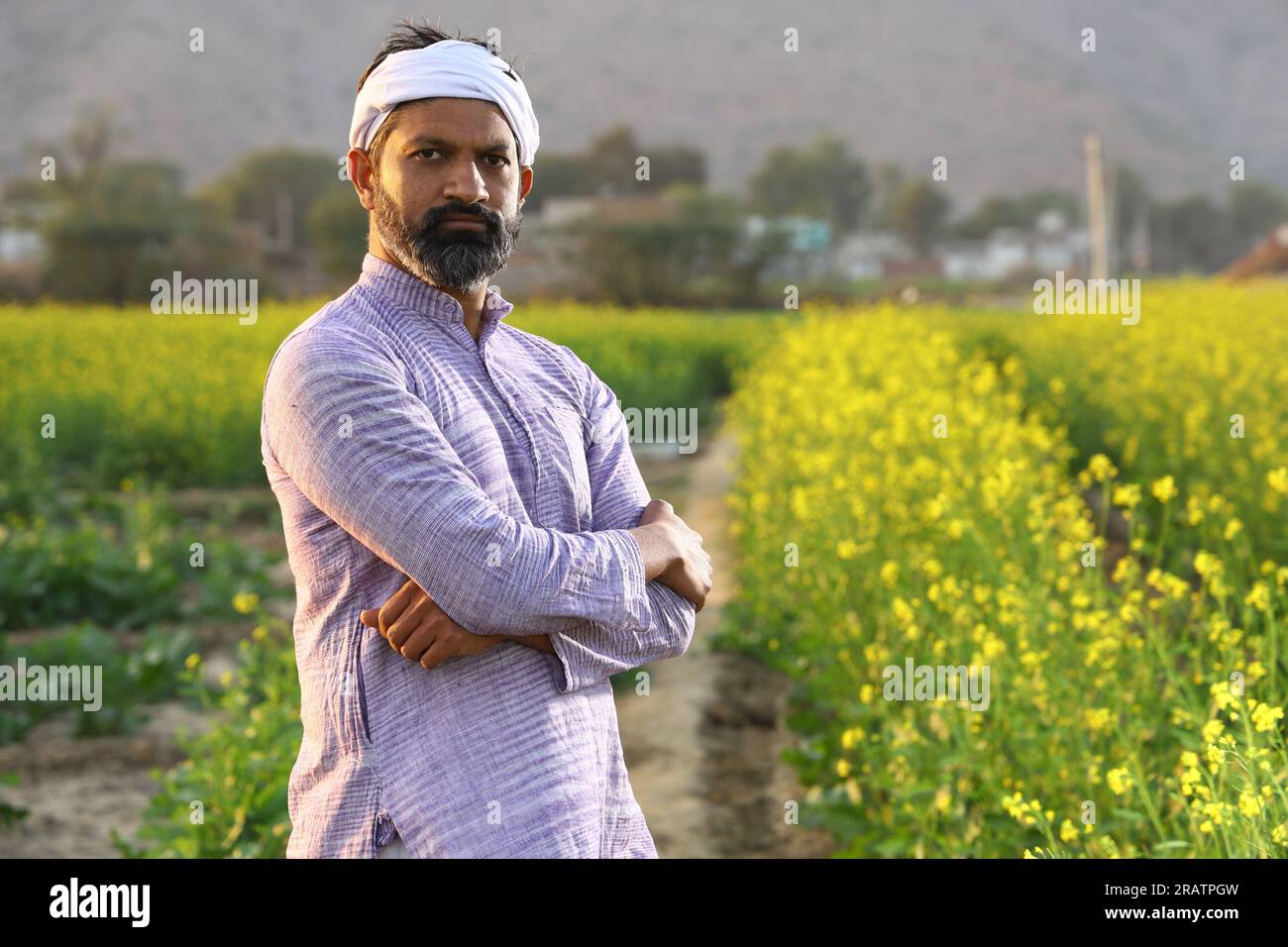 Agricoltore che si sente orgoglioso del suo impegno per la crescita del suo campo. Bellissimo ritratto di un contadino rurale indiano in piedi nel campo di senape. Foto Stock