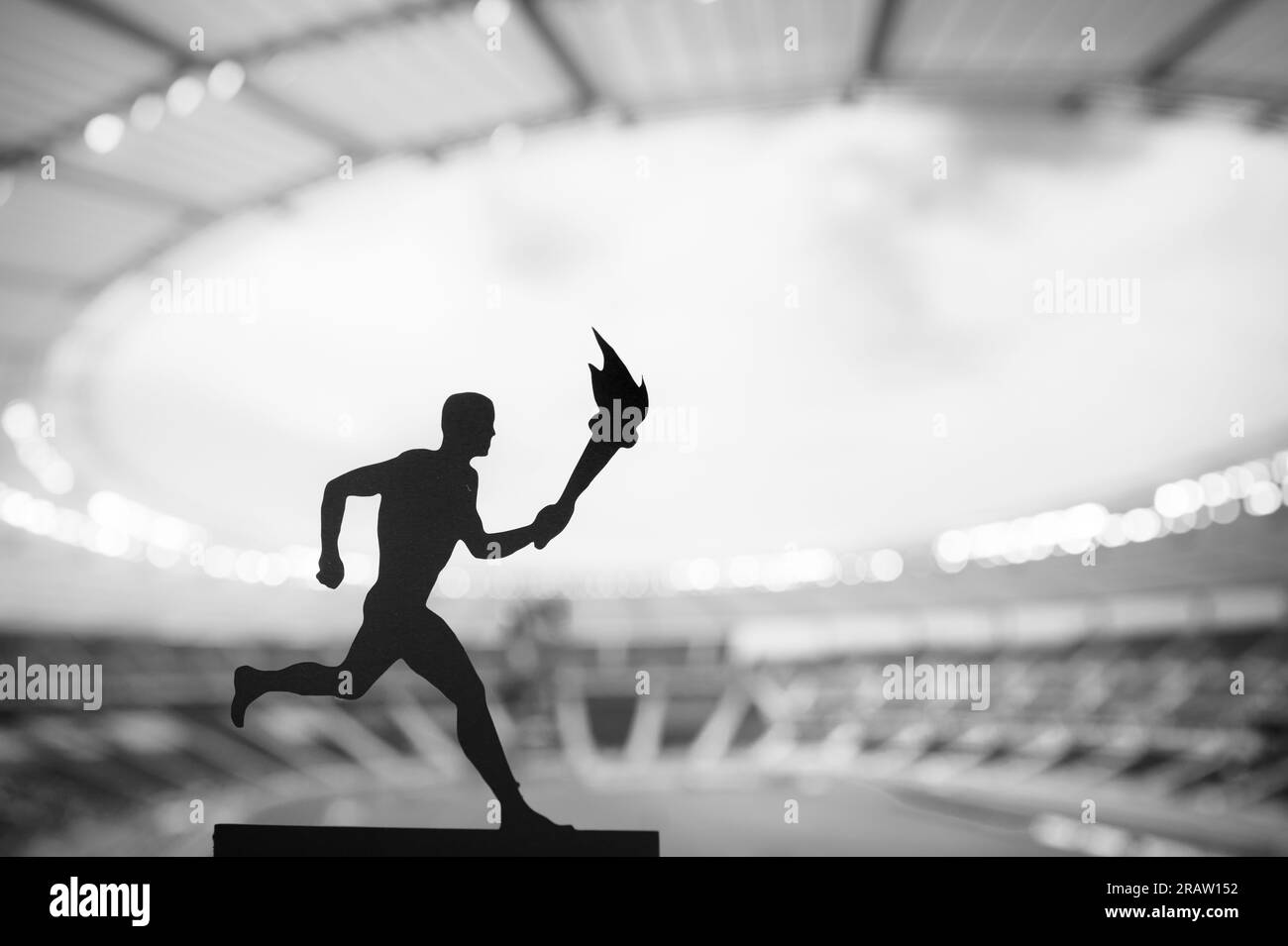 Passing the Flame: Silhouette di atleta maschile in Torch Relay, contro un moderno stadio di atletica leggera. Un'immagine potente per l'evento estivo 2024 Foto Stock