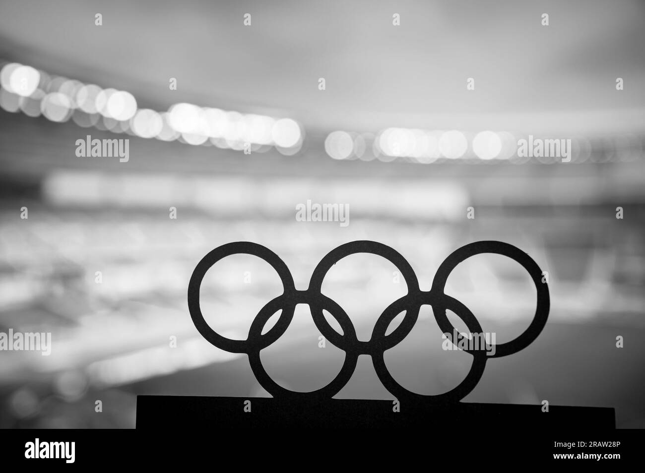 PARIGI, FRANCIA, 7 LUGLIO 2023: Foto in bianco e nero. Silhouette degli anelli olimpici che abbracciano un moderno stadio olimpico sullo sfondo. Paris Summer Oly Foto Stock