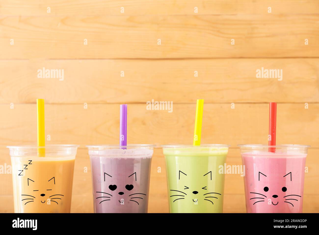 Tazze di plastica di gustosi cocktail colorati con emoticon di gatto disegnate su sfondo di legno Foto Stock