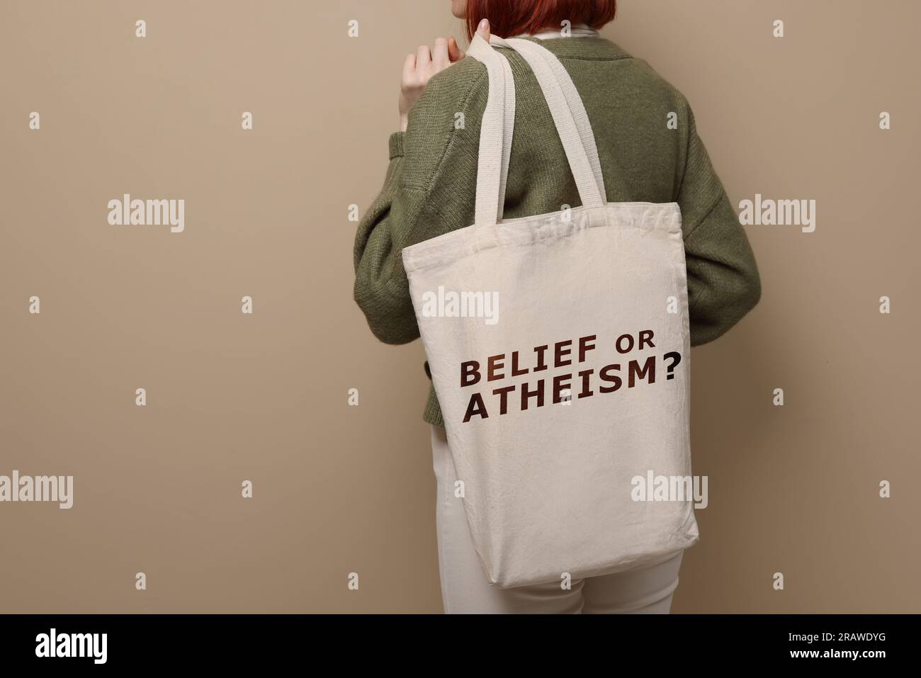 Donna che tiene la borsa con frase credenza o ateismo? su sfondo beige, primo piano Foto Stock