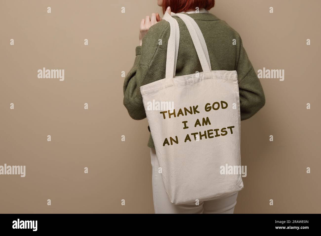 Donna che tiene la borsa con la frase Grazie a Dio sono ateo su sfondo beige, primo piano Foto Stock