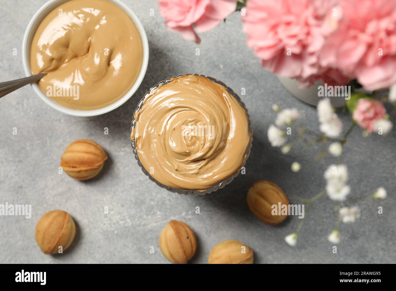 Bicchiere di delizioso caffè dalgona, ingredienti e biscotti a forma di noce su un tavolo grigio chiaro, piatto Foto Stock