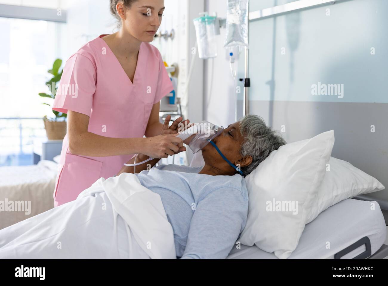 Medico femminile diversificato e paziente anziano che indossa la maschera di ossigeno in ospedale. Ospedale, medicina e servizi sanitari, inalterati. Foto Stock