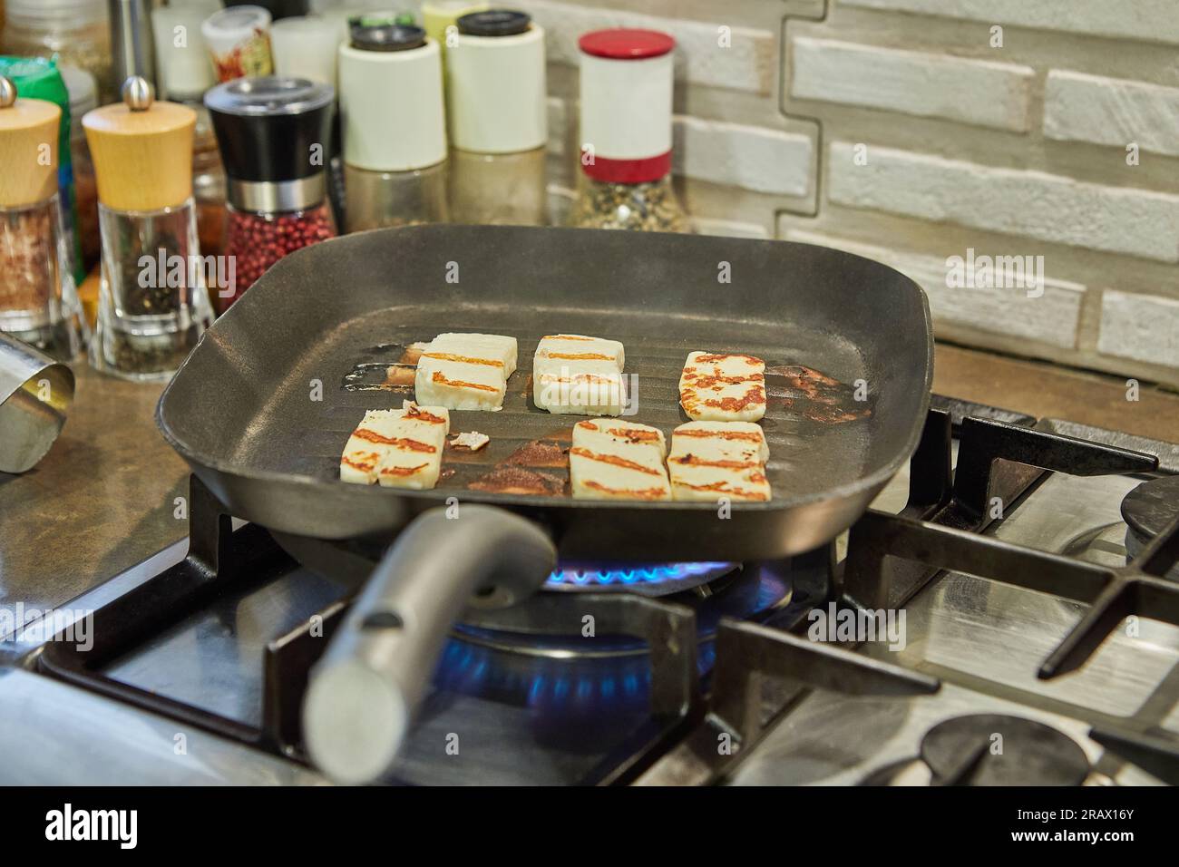 Il formaggio halloumi viene fritto su una teglia a coste sul fuoco sulla stufa a gas. Foto Stock