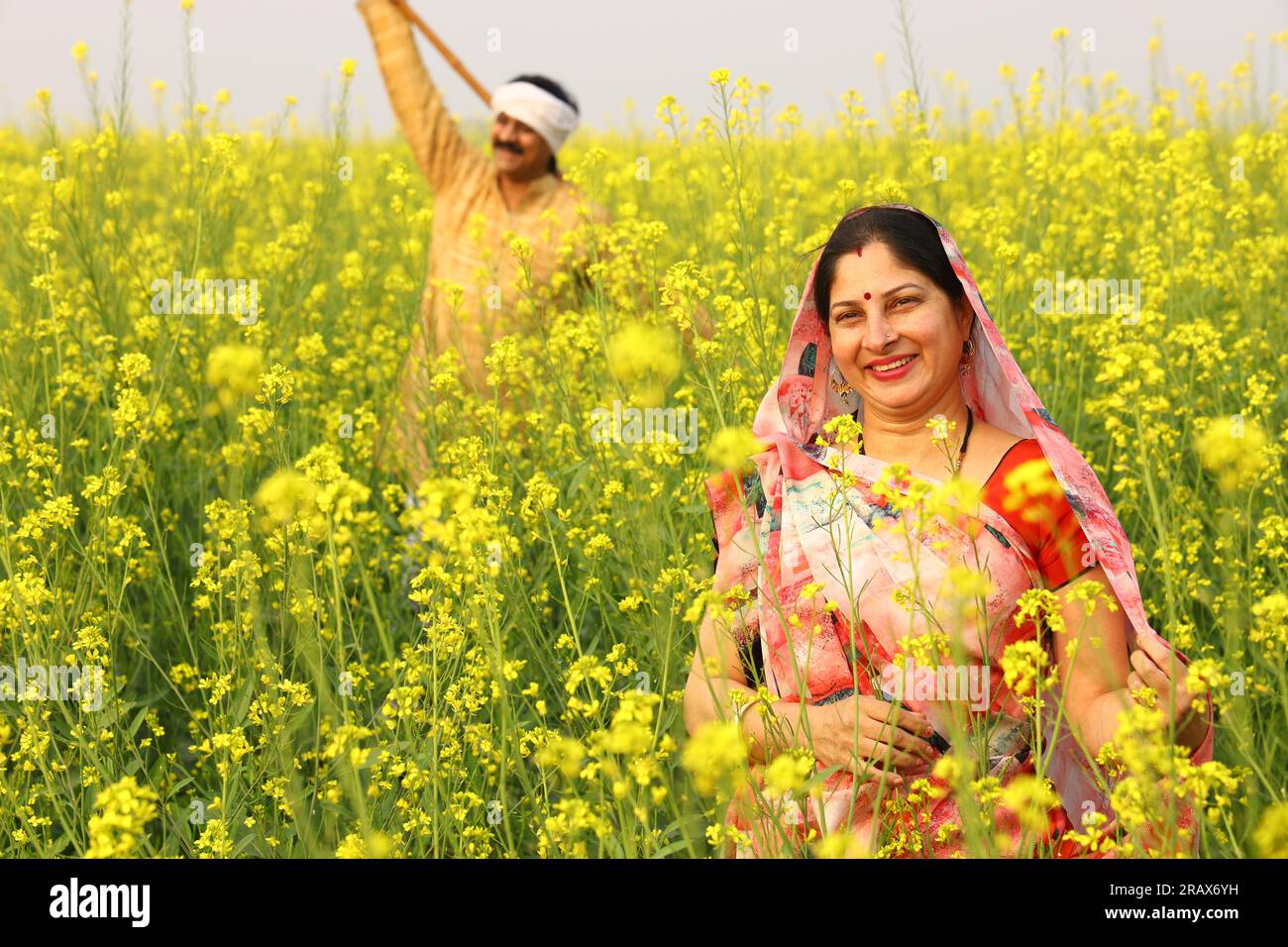 Famiglia rurale indiana che si trova nel campo della senape e marito e moglie sono felici di vedere i benefici agricoli del campo. Foto Stock