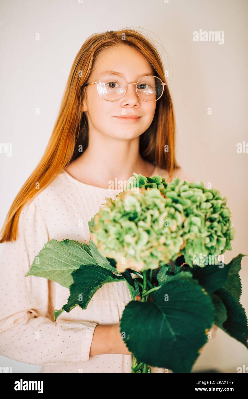 Ritratto di una dolce bambina con i capelli rossi, che indossa occhiali da vista, che regge un fiore di ortensia verde Foto Stock