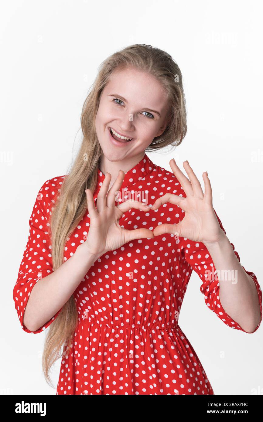 Ritratto di una giovane donna bionda confessa innamorata, fa gesto cardiaco con entrambe le mani e guarda la fotocamera, mostrando sentimenti veri su sfondo bianco Foto Stock