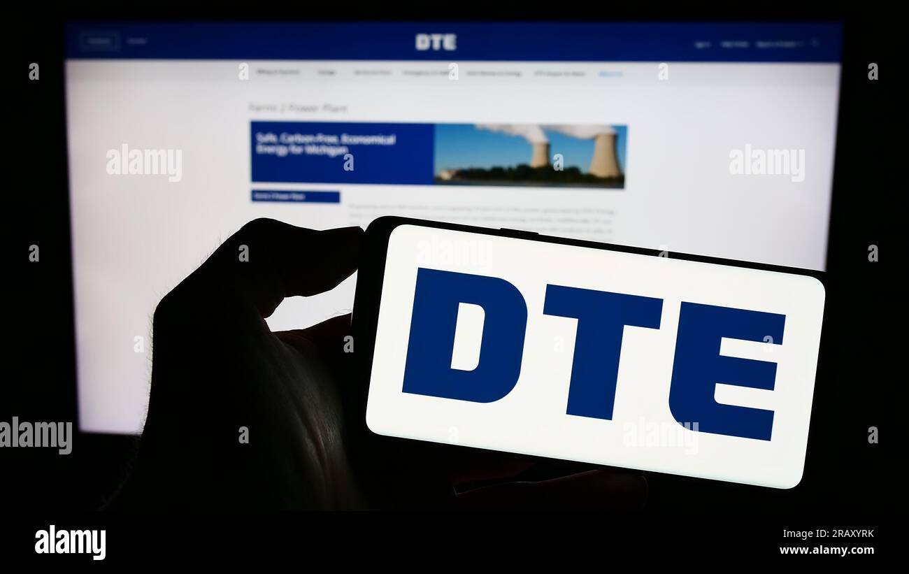 Persona che possiede il cellulare con il logo della società di servizi pubblici statunitense DTE Energy Co. Sullo schermo davanti alla pagina Web aziendale. Concentrarsi sul display del telefono. Foto Stock