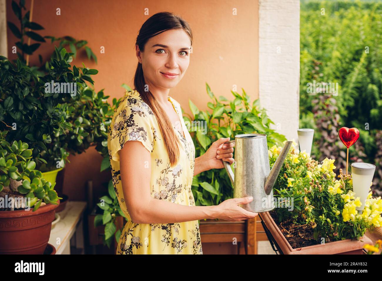 Ritratto di bella donna annaffiando piante verdi sul balcone, piccolo giardino accogliente in appartamento Foto Stock