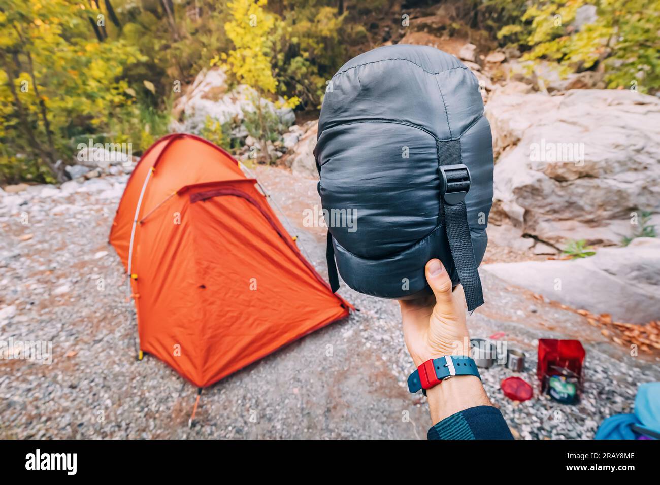 Borsa a compressione piccola e leggera con sacco a pelo in piuma sullo sfondo di una tenda in campeggio e varie attrezzature e oggetti da campeggio Foto Stock