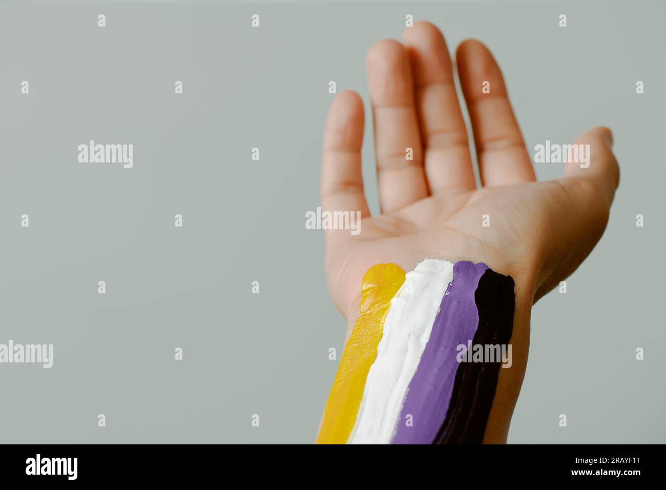 primo piano del braccio di una giovane persona caucasica con la bandiera di orgoglio non binario dipinta su uno sfondo grigio pallido Foto Stock