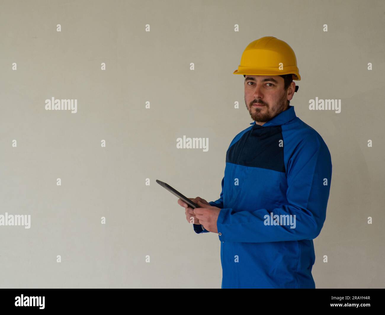 Ritratto del lavoratore o dell'ingegnere in abiti da lavoro blu e casco di sicurezza giallo con spazio per il testo. Un uomo in un cantiere tiene un tablet nella sua h Foto Stock