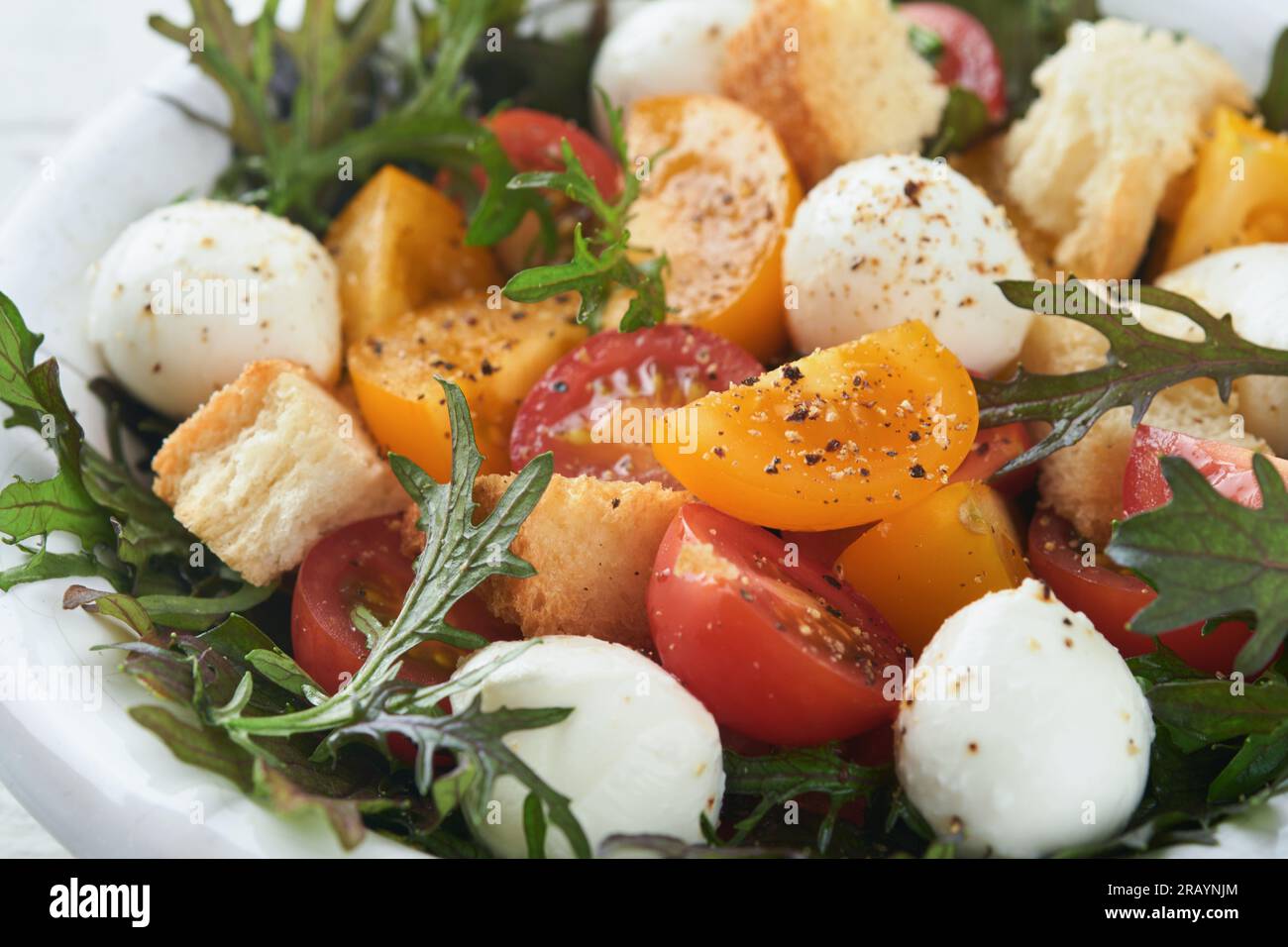 Panzanella toscana. Insalata di pomodori ciliegini con rucola, basilico, mozzarella e cracker di pane su recipiente bianco. Insalata tradizionale italiana. Mediterraneo lui Foto Stock