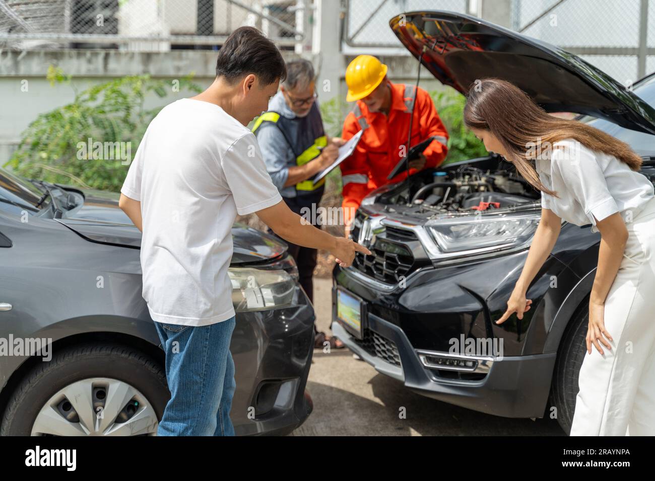 Un uomo e una donna che puntano i segni di graffio sulla macchina dell'incidente, mentre un agente di assicurazione auto e un machanic ispezionano la macchina dalla ot Foto Stock