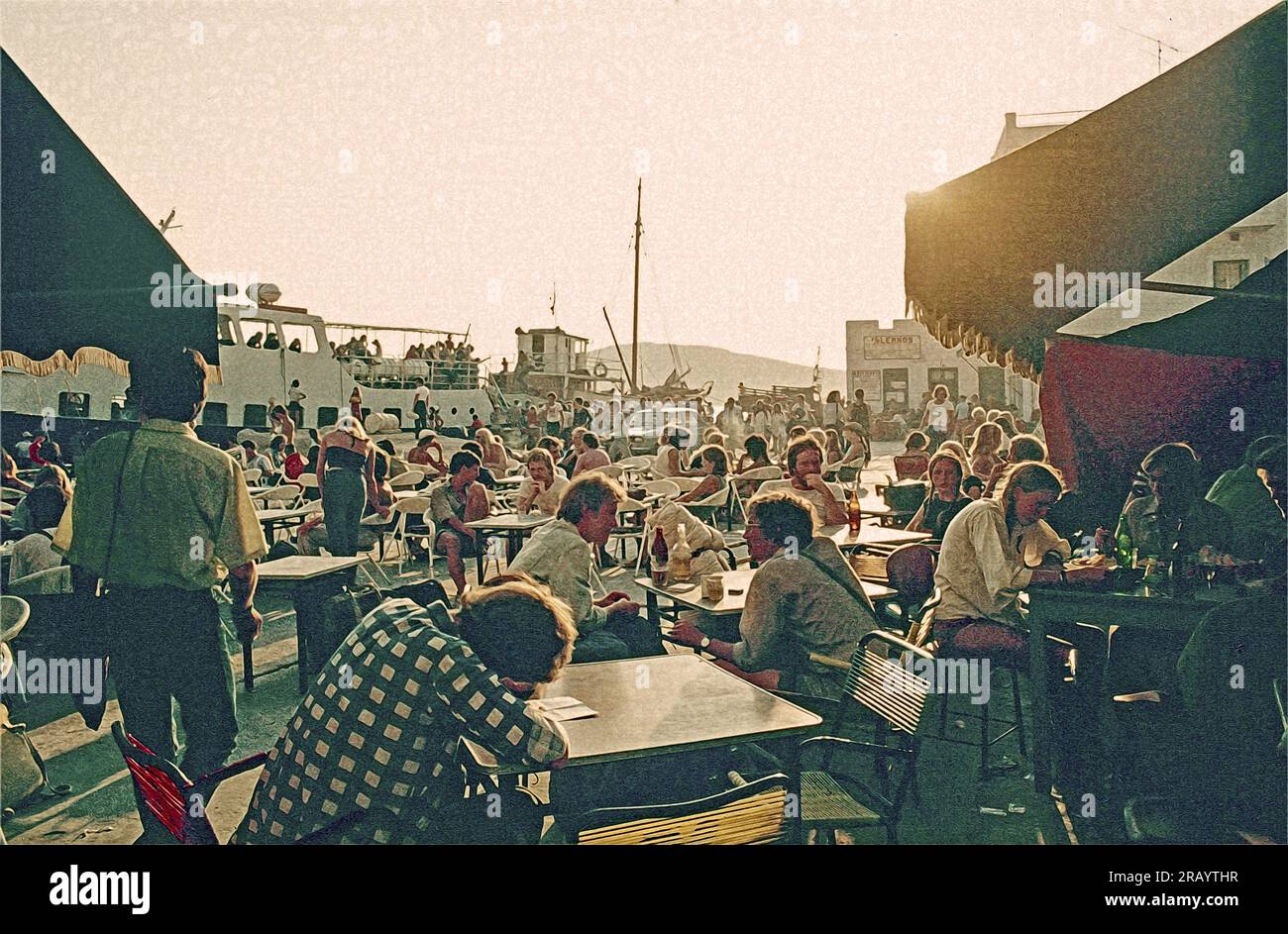 Foto di una piazza del caffè al porto di iOS nelle Cicladi, Grecia 1976. Persone che si incontrano per un drink serale o qualcosa da mangiare Foto Stock