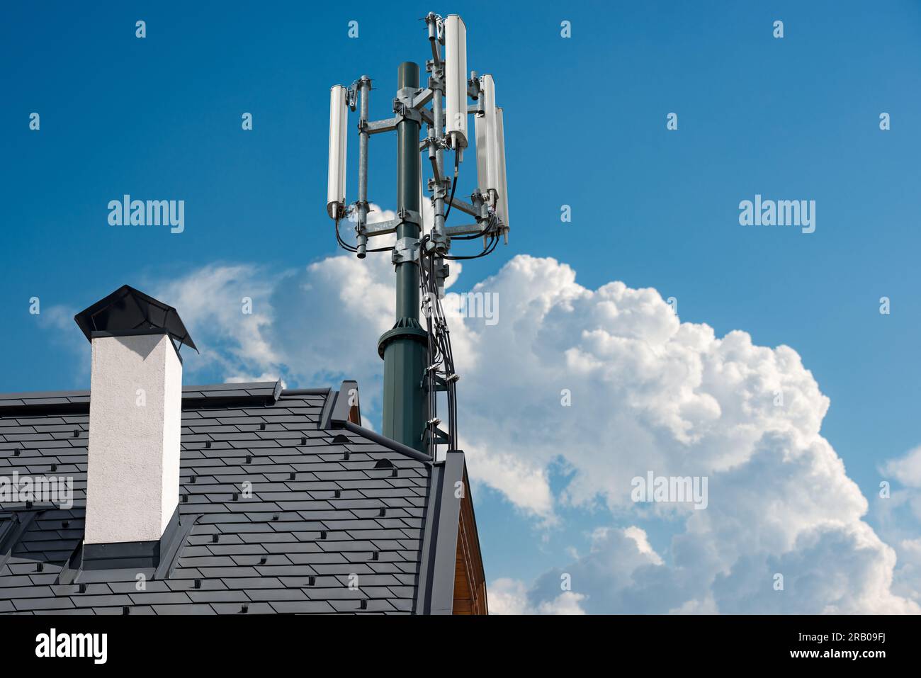 Primo piano del tetto di una casa con una torre di telecomunicazioni con antenne, contro un cielo azzurro con nuvole e spazio di copia. Foto Stock