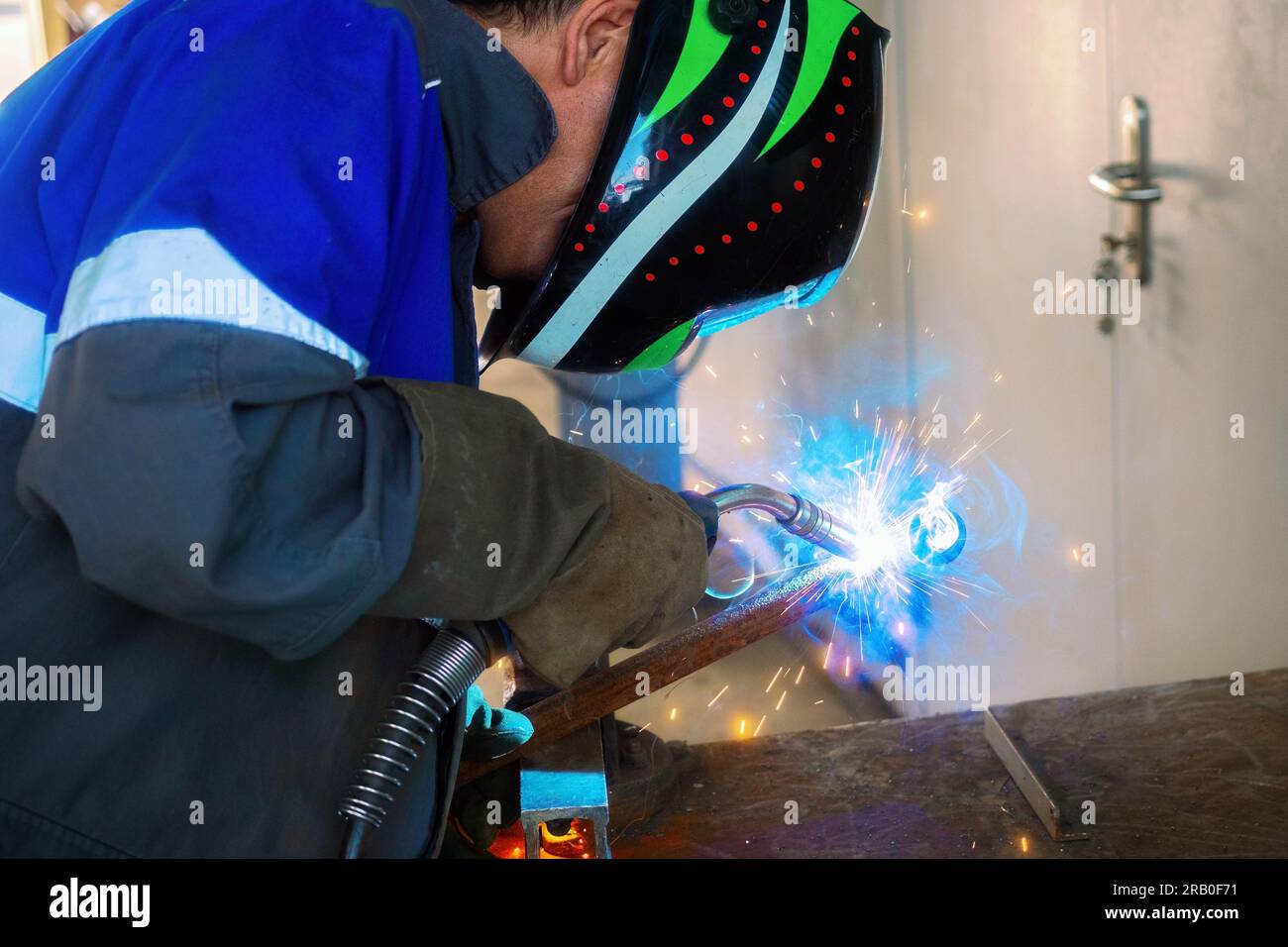 Saldatore al lavoro. Saldatore professionale in maschera di protezione salda tubi metallici in officina di produzione e scintille. Background industriale. Foto Stock