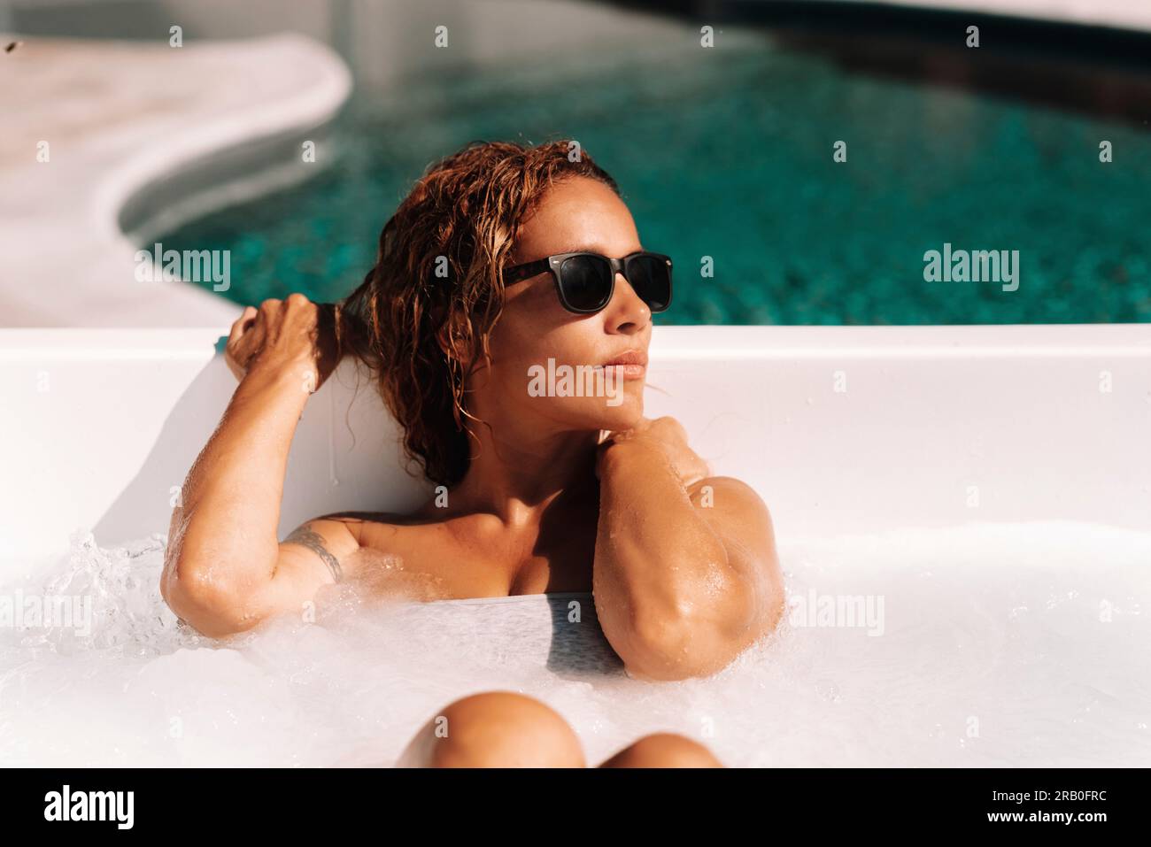 Una giovane donna adulta attraente gode di tubo idromassaggio e di sole giornate di vacanze estive rilassandosi e curando il corpo. Stile di vita delle persone di lusso. Una donna elegante che si rilassa nella piscina in giardino o nella spa Foto Stock