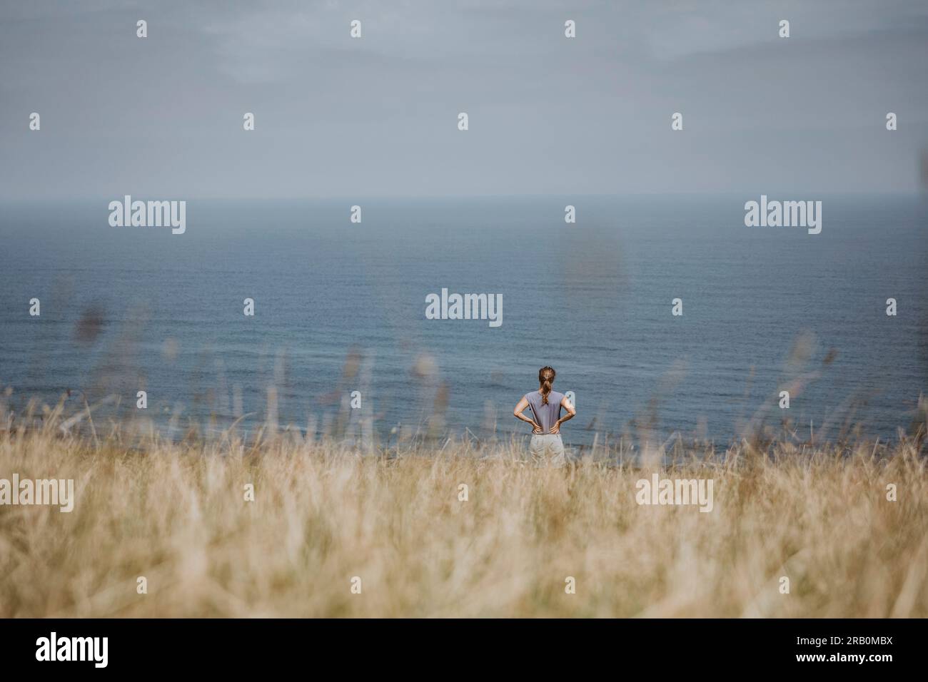 Donna in piedi sul prato che guarda il mare, Spagna Foto Stock