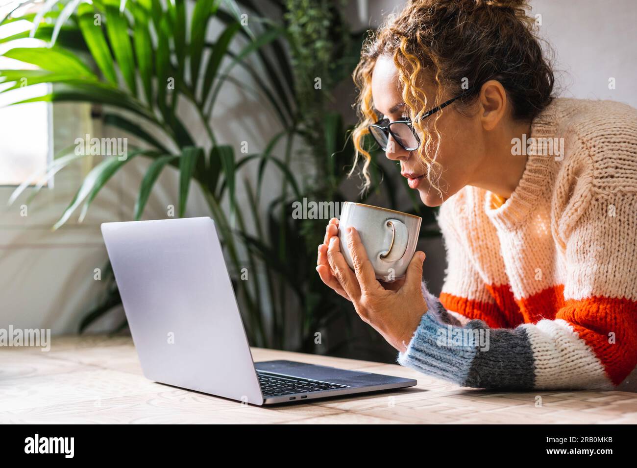 Ritratto di giovane imprenditore maturo che utilizza il computer portatile da solo in ufficio bevendo tè per uno stile di vita sano. Donne che indossano occhiali da vista e navigano in rete sul computer con connessione wireless Foto Stock