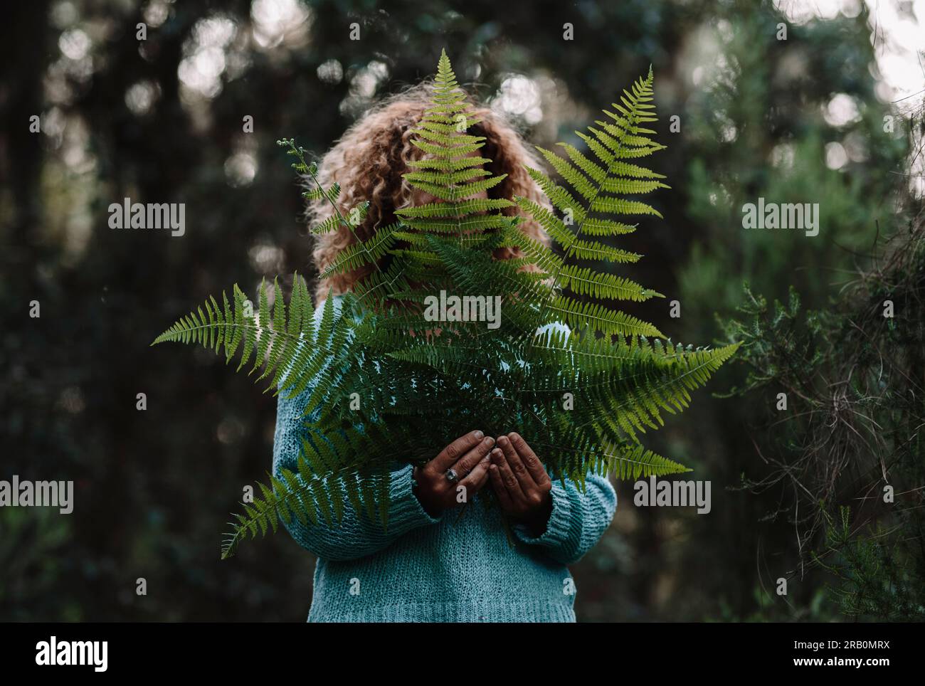 Ritratto di foglie verdi e donna che si tiene contro il volto. Concetto di stile di vita sano persone e connessione con la natura all'aperto. Donna in attività ricreative all'aperto da sola nel bosco di fondo Foto Stock