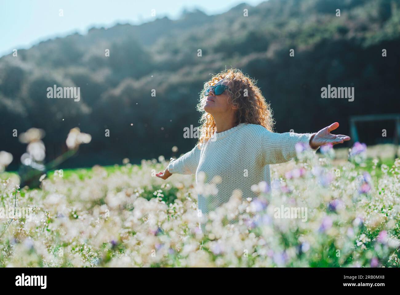 Donna che si gode un campo estivo con fiori bianchi in fiore. Stile di vita sano e libertà concetto di persone. Attività ricreative all'aperto piacevoli. Lady che si gode il parco naturale estivo e la destinazione turistica Foto Stock