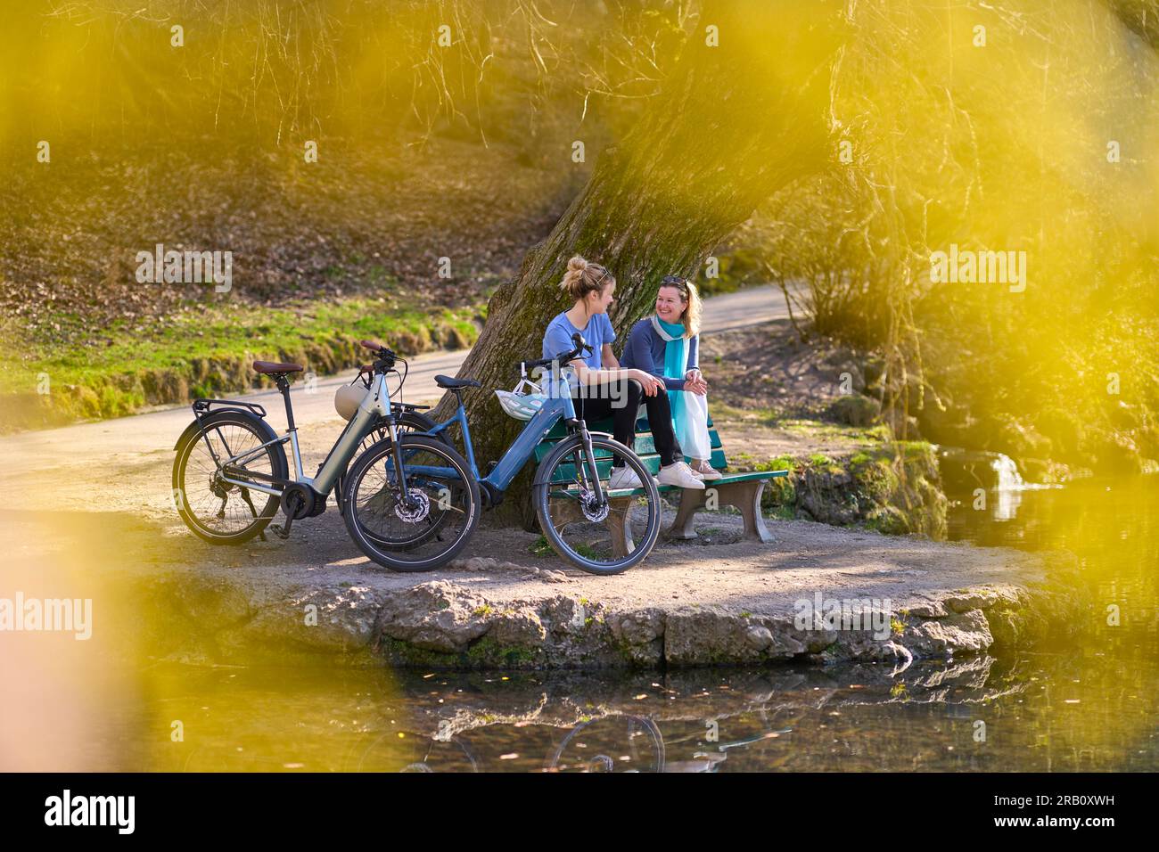 Due donne con e-bike fanno una pausa in uno stagno nel parco cittadino, in primavera Foto Stock