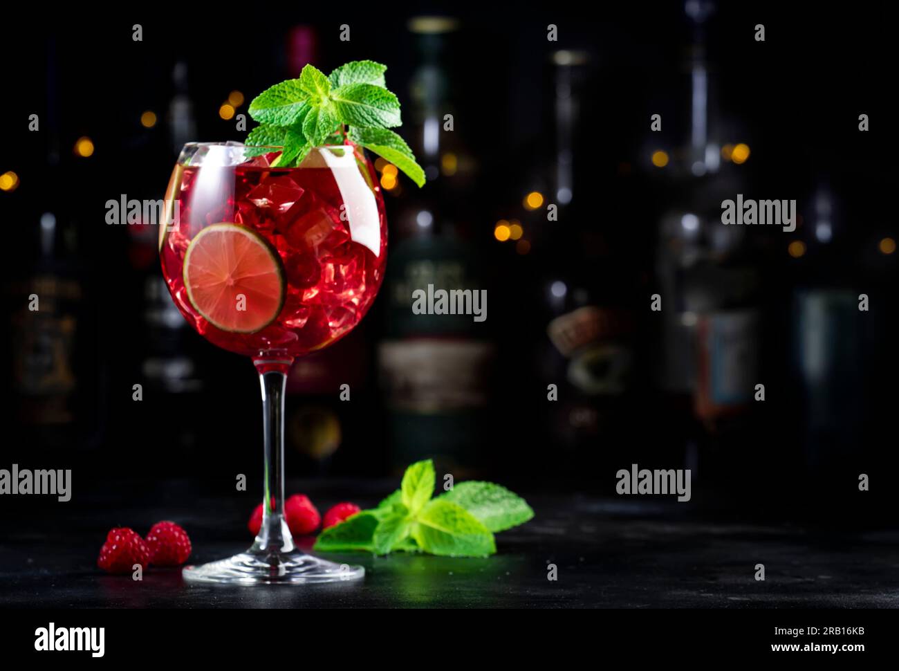 Cocktail alcolico Royal limonade con tequila, gin secco, rum bianco, vodka, liquore, lime, lamponi e ghiaccio nel bicchiere da vino. Bancone bar nero ba Foto Stock