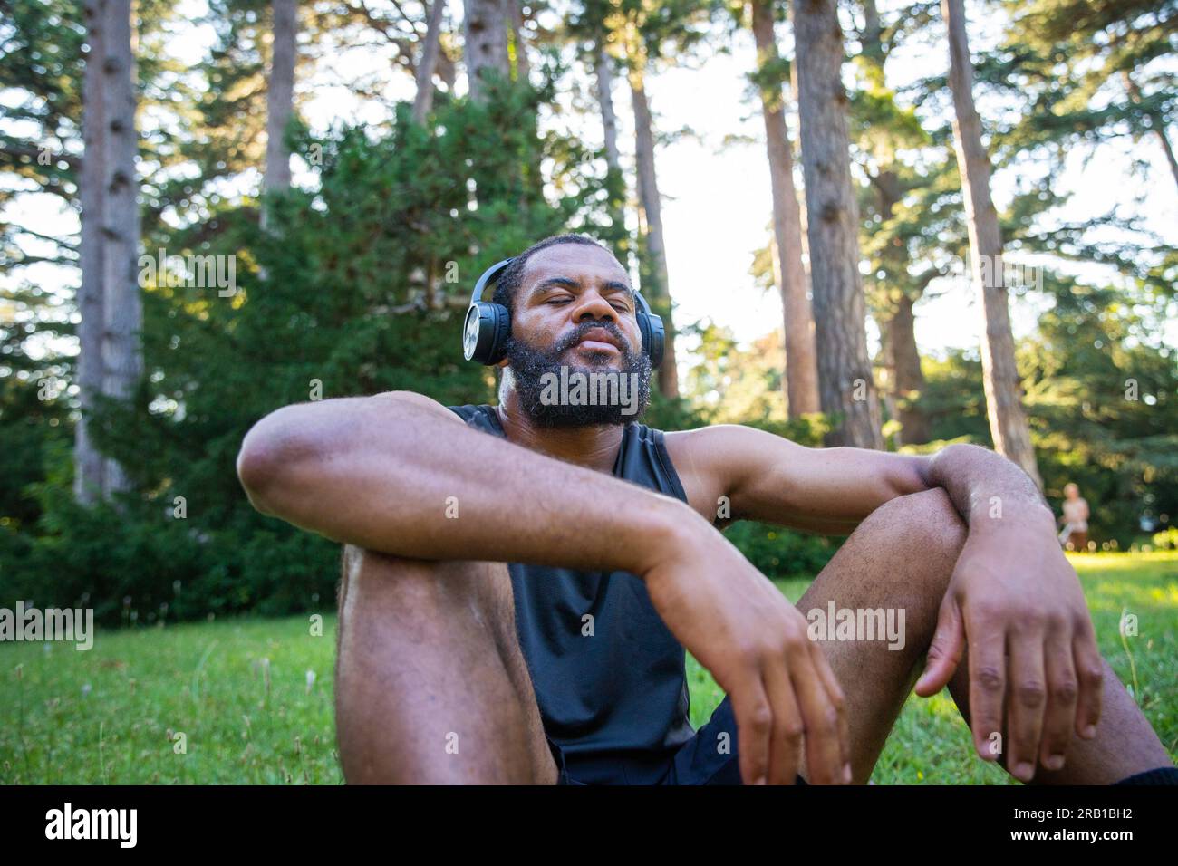 Un atleta si rilassa dopo un allenamento e ascolta la musica respirando aria fresca con gli occhi chiusi. Foto Stock