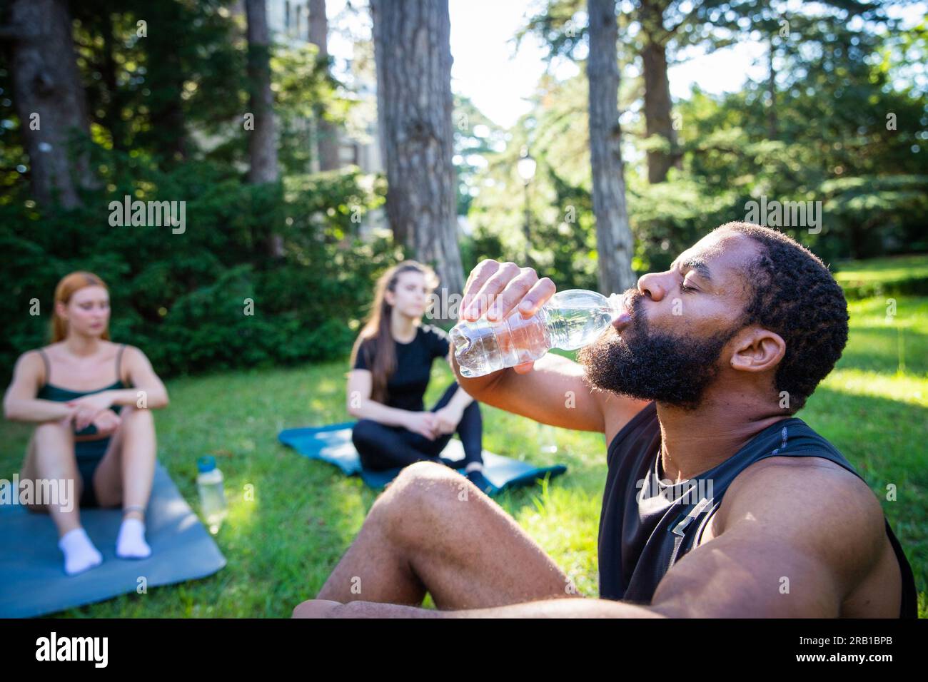 Un atleta beve acqua durante un allenamento in un parco pubblico, idratazione durante lo sport Foto Stock